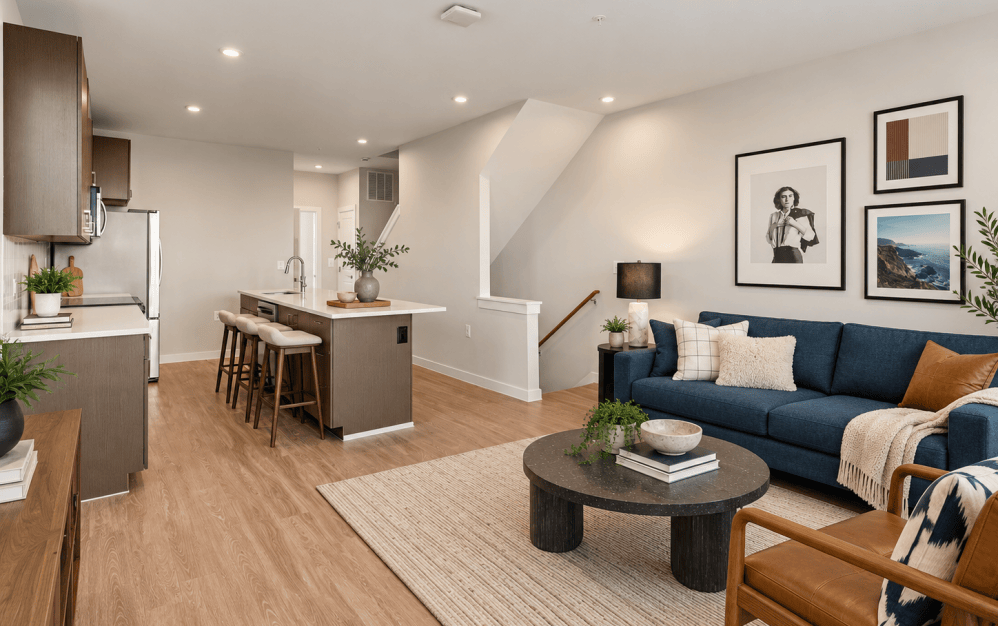 Staged C4 open-concept living room and kitchen at Alta NOVA featuring a blue sofa, contemporary furnishings, wood-style flooring, kitchen island, and modern finishes.