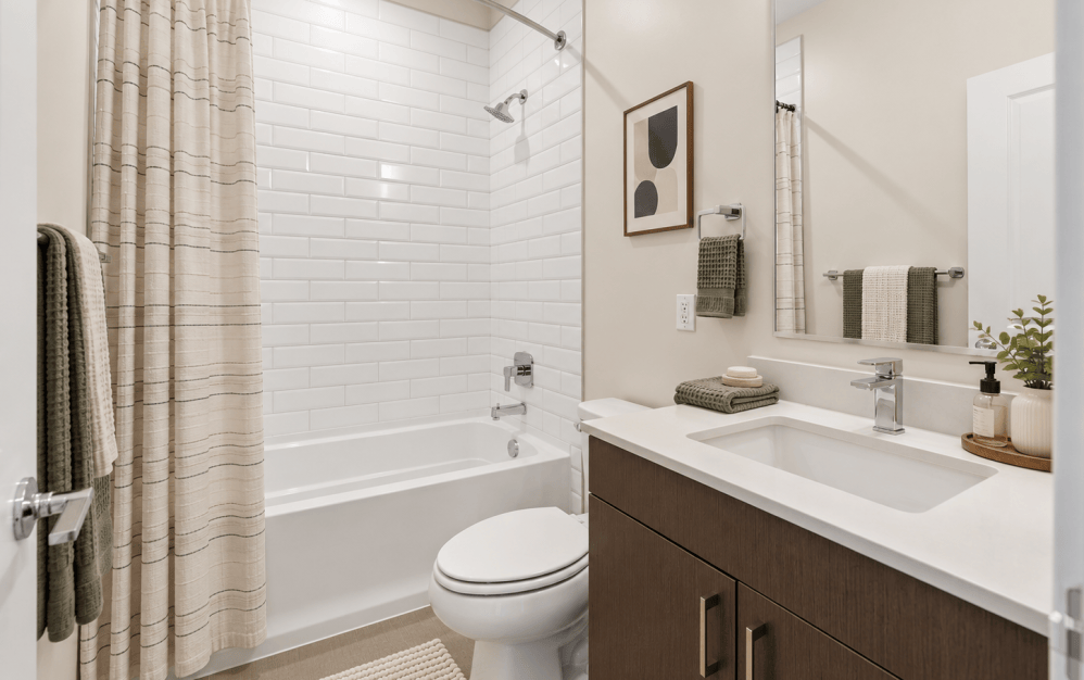 Staged C4 bathroom at Alta NOVA featuring a modern vanity with quartz countertop, dark wood cabinetry, white subway tile bathtub surround, and contemporary fixtures.