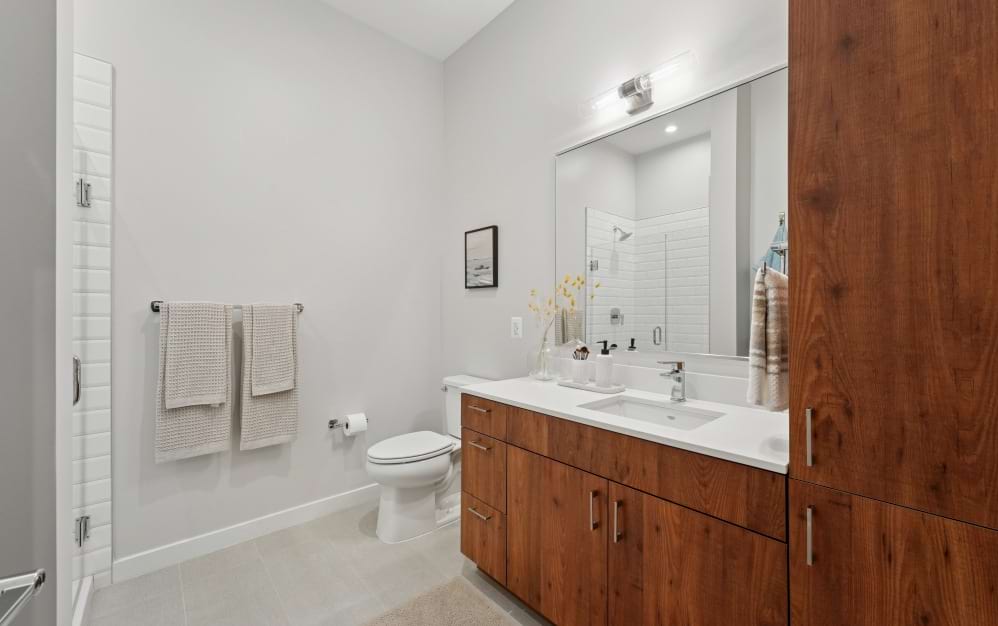 A8 apartment bathroom at Alta NOVA featuring a spacious vanity, wood cabinetry, large mirror, and tiled shower.