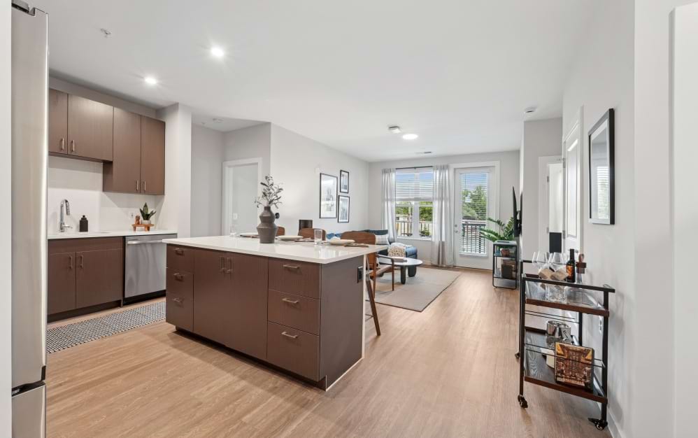 Open-concept A9 apartment at Alta NOVA in Falls Church, VA, featuring a spacious kitchen island, wood cabinetry, stainless steel appliances, and a bright living area with balcony access.