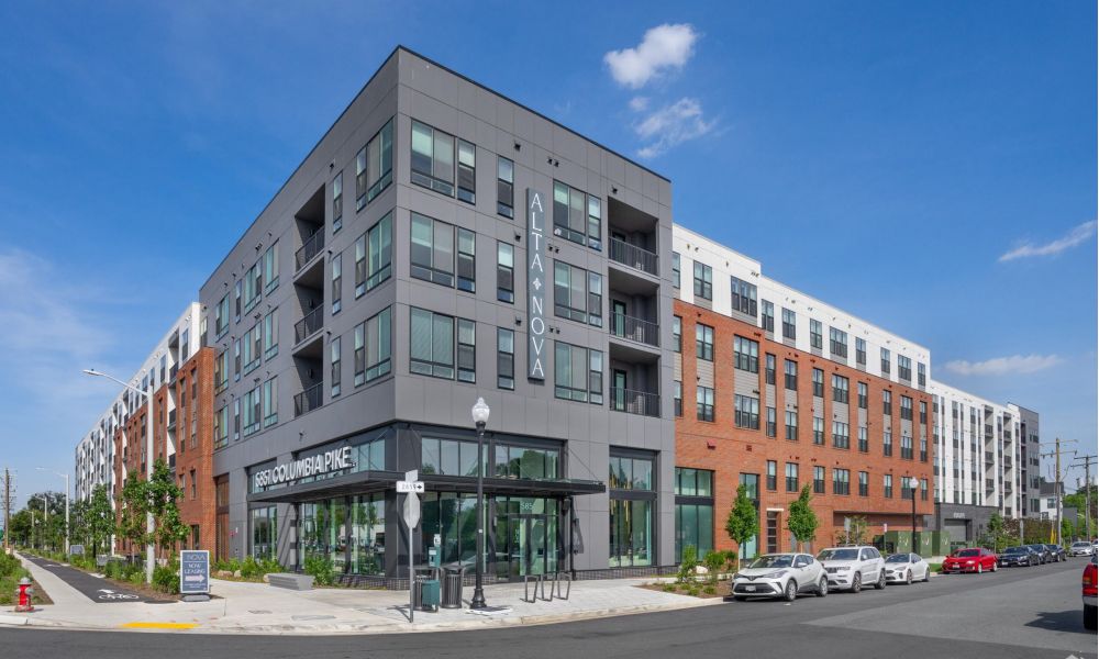 Alta Nova modern apartment building with gray and red brick exterior on a sunny day, with shops at street level.