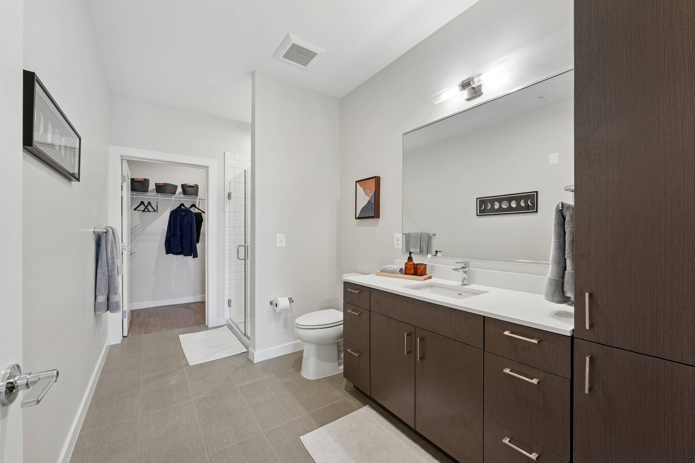 Alta Nova apartments Modern bathroom with dark wood cabinets, large mirror, glass shower, and neutral-toned decor.