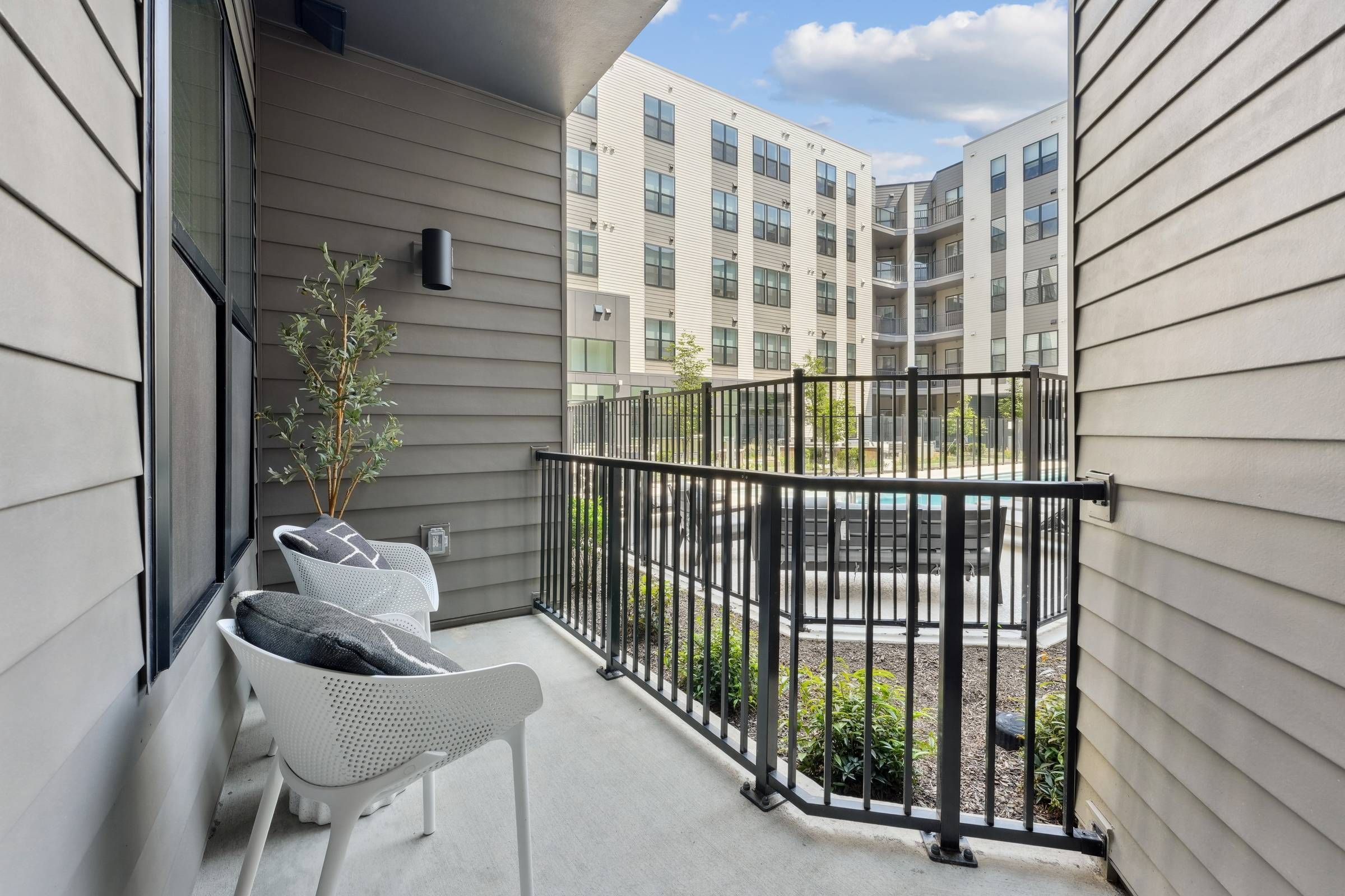 Alta Nova apartments Small apartment balcony with two chairs and a plant, overlooking a courtyard and modern apartment buildings.