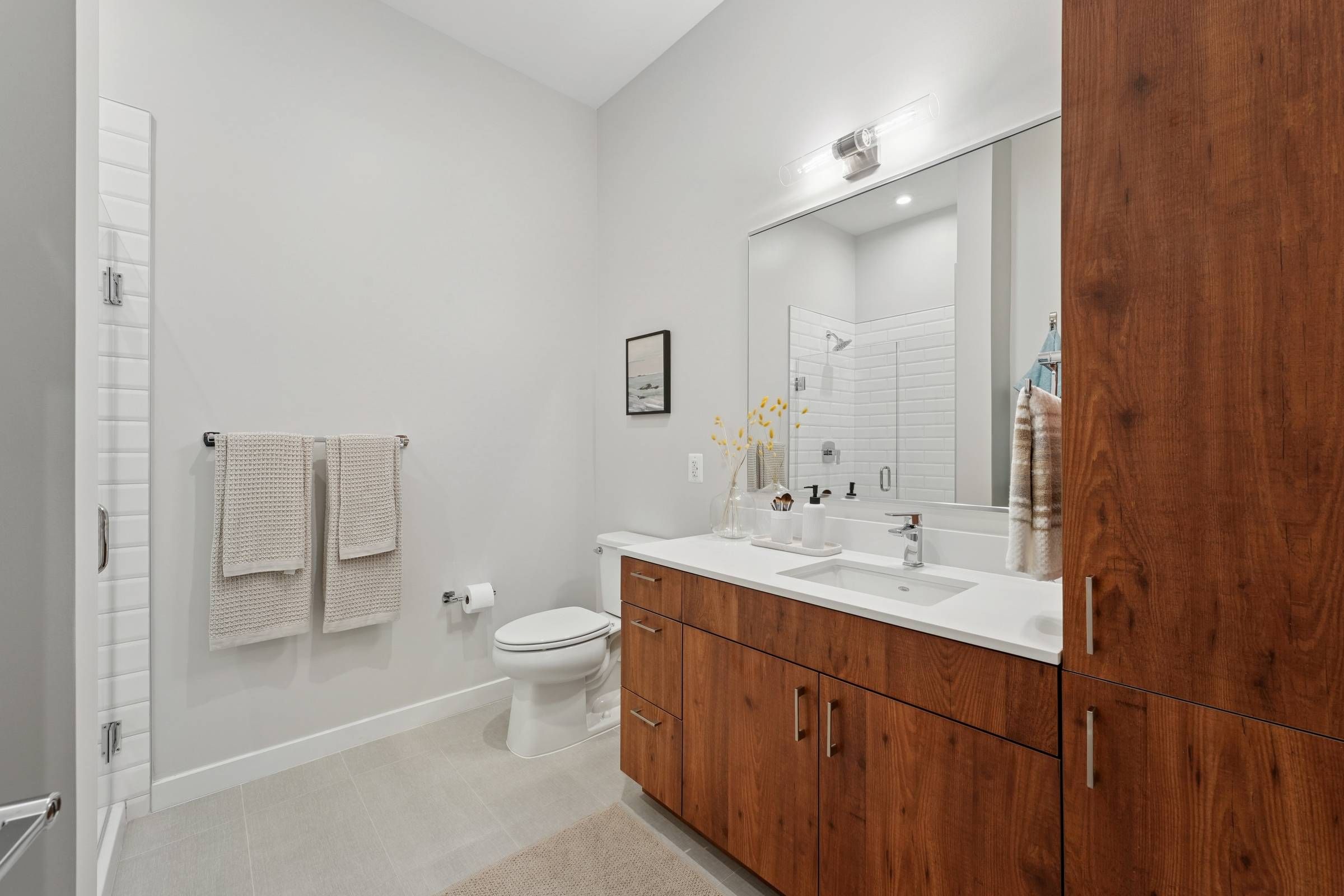 Alta Nova apartments Modern bathroom with wooden cabinets, double sink, large mirror, and white towels hanging by the toilet.