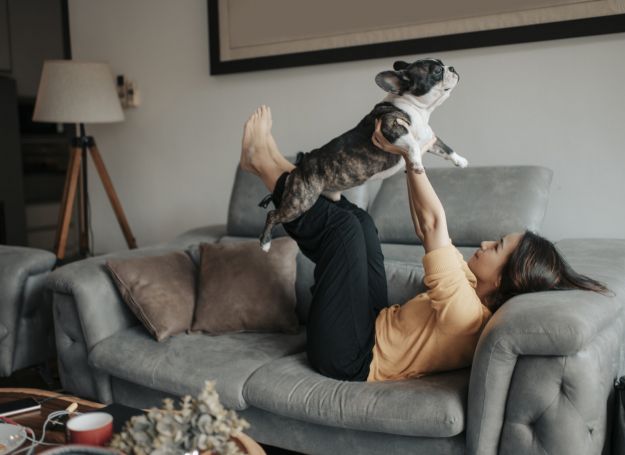 Alta Nova Apartments woman on grey couch raising dog in her arms