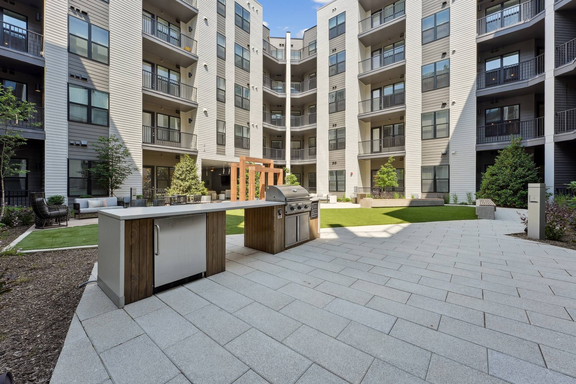 Alta Nova apartments Modern apartment courtyard with outdoor kitchen, BBQ grill, green lawn, and surrounding balconies.